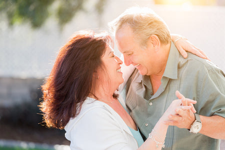 A happy senior couple dancing and smiling at each other, exuding joy and closeness in a sunlit setting.
