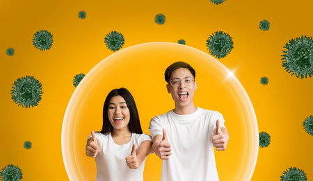 Two cheerful people giving thumbs up, protected by a shield symbolizing immunity, with illustrated green viruses in the background.